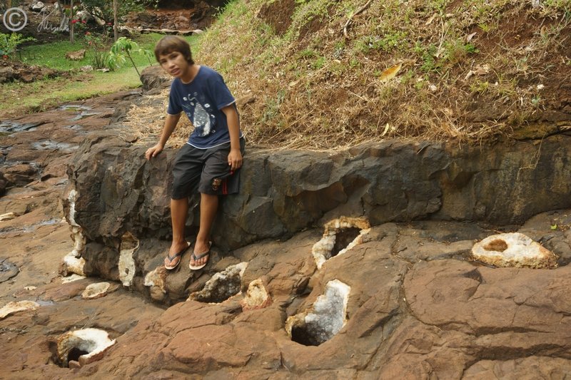 Sohn des Besitzers erklärt uns die Schmucksteinmine vor einer Fundstätte mit geöffneten Drusen